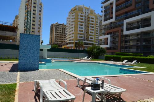 a swimming pool with two lawn chairs and two buildings at ROCHA Tower 4D in Portimão
