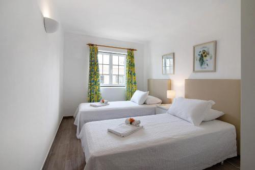 two beds in a room with white walls and a window at Apartamento Old Village T2 Duplex in Quarteira