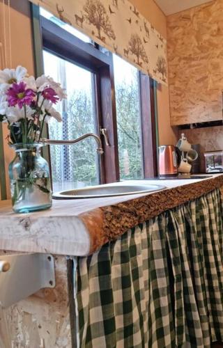 a kitchen counter with a vase with flowers on it at The Woodland Lodge - Wood Fired Hot Tub and Firepit in Hambleton