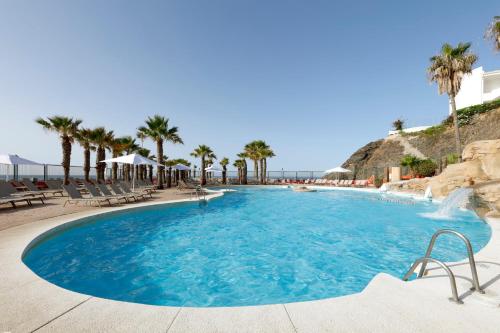 a large swimming pool with chairs and palm trees at Hotel Benalma Costa del Sol in Benalmádena