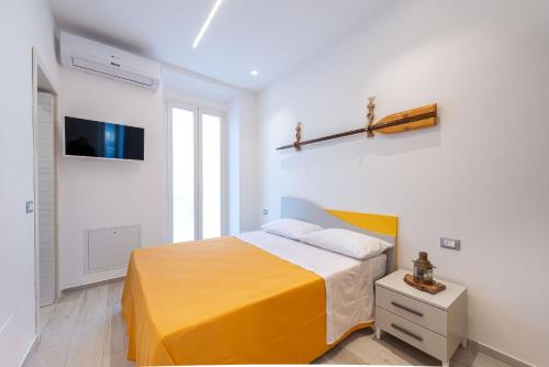 a white bedroom with a yellow bed and a tv at La Retara Affittacamere in San Benedetto del Tronto