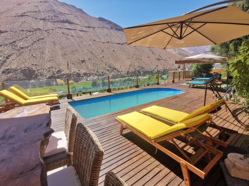 a deck with chairs and an umbrella and a swimming pool at Lodge Nueva Elqui in Pisco Elqui