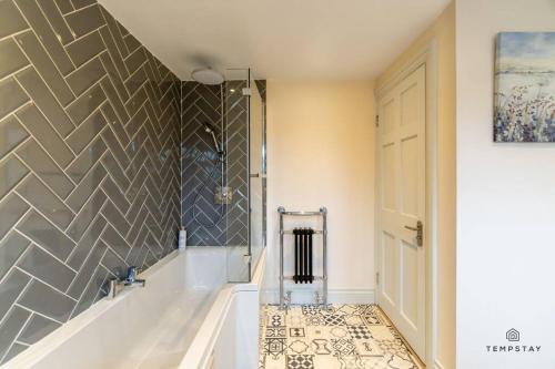 a bathroom with a tub and a shower with a tile wall at STYLISH HOME WITH FREE PARKING - 10 MINS TO LEGOLAND! in Windsor