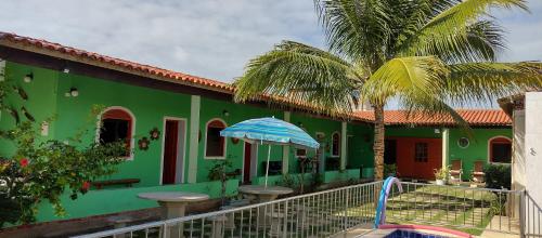 a green house with a palm tree and an umbrella at POUSADA LUATOUR Praia Pontal do Coruripe in Coruripe