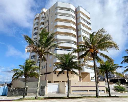 een hoog wit gebouw met palmbomen ervoor bij Frente pro mar apartamento completo in Praia Grande