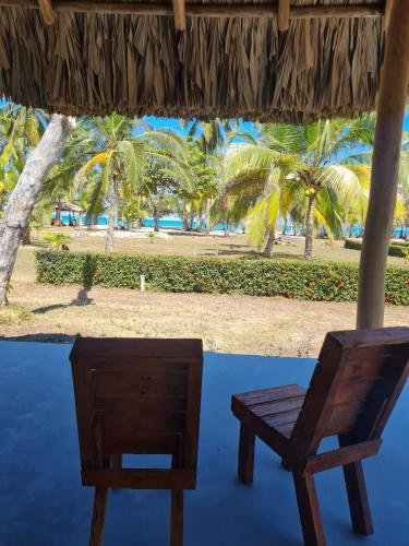 two chairs sitting under a porch with palm trees at Hotel Playa Mandala in Palomino