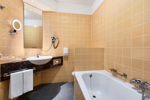 a bathroom with a bath tub and a sink and a mirror at NH Zoetermeer Hotel in Zoetermeer