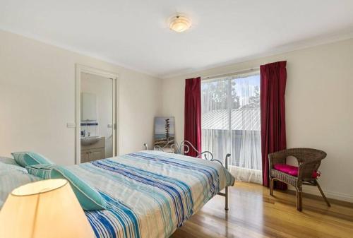 um quarto com uma cama, uma cadeira e uma janela em Phillip Island Time - Large home with self-contained apartment sleeps 11 em Cowes