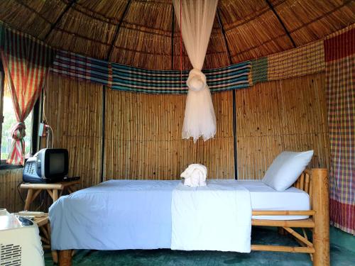 a bed in a straw room with a tv at Saengcha Farm Resort in Prachin Buri