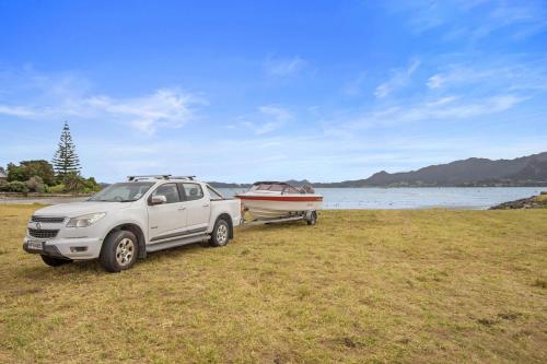 a white truck parked next to a boat on a field at The Sunrise Bach - One Tree Point Holiday Home in One Tree Point
