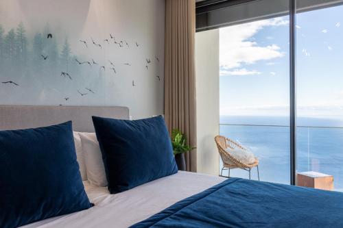 a bedroom with a bed with blue pillows and a window at The Cliffhouse by LovelyStay in Fajã da Ovelha