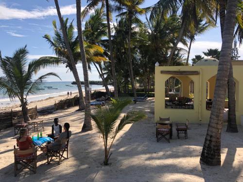 people sitting at tables on a beach with palm trees at Sawa Sawa Beach House in Msambweni