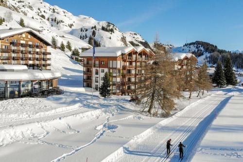 zwei Personen Skifahren im Schnee vor einem Hotel in der Unterkunft Rhodania 55 in Riederalp