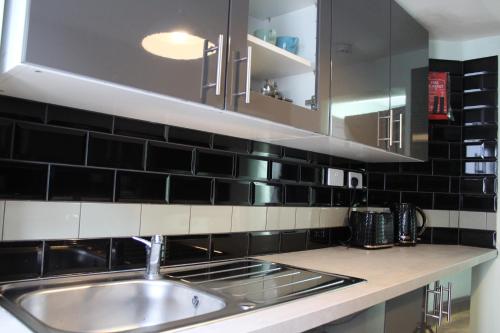 a kitchen with a sink and black tiles on the wall at Vacation Home - Garden, Netlfix, Wifi. in Margate