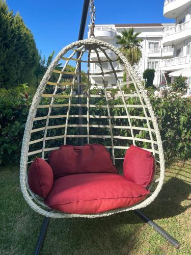 a hanging chair with a red cushion in a yard at BELKA GOLF RESİDENCE Luxury Apt Poolside Belek in Belek