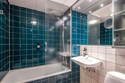 uma casa de banho com azulejos azuis, um lavatório e um chuveiro em Comwell H C Andersen Dolce by Wyndham em Odense