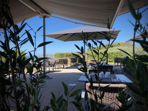 a patio with tables and chairs and an umbrella at Logis Hôtel & Restaurant LES MOUETTES - Larmor Plage, Proche de LORIENT in Larmor-Plage