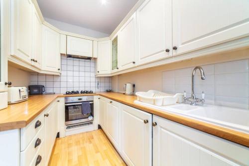 Amazing 1BD in Victorian house - Lewisham Park في لندن: مطبخ مع دواليب بيضاء ومغسلة