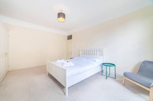Amazing 1BD in Victorian house - Lewisham Park في لندن: غرفة نوم بيضاء بسرير وكرسي ازرق