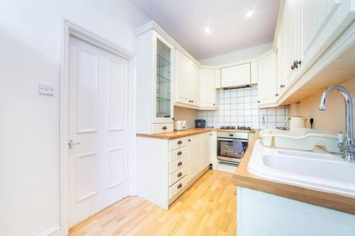 Amazing 1BD in Victorian house - Lewisham Park في لندن: مطبخ بدولاب بيضاء ومغسلة كبيرة