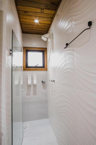 a white bathroom with a shower and a window at Pousada Colina Verde in Garopaba