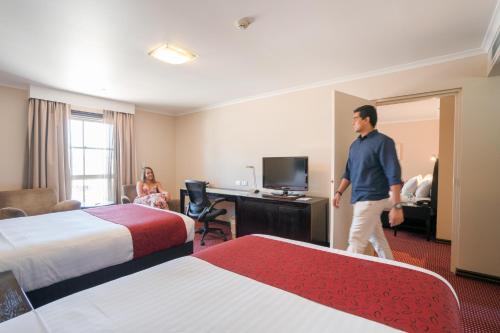 a man is standing in a hotel room with two beds at Hotel Grand Chancellor Launceston in Launceston
