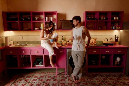 a man and woman standing in a pink kitchen at Casa Nicté, hospédate en una casa del siglo XVIII in Campeche