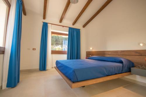 1 dormitorio con 1 cama con cortinas azules y ventana en Villa Corbezzolo (Country House) en Dorgali
