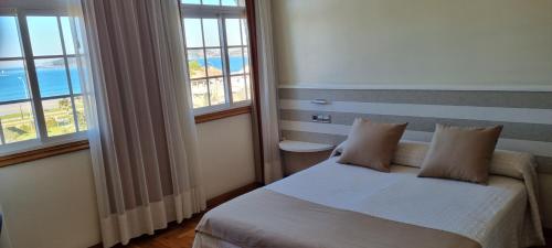 a bedroom with a bed with two pillows and two windows at Hotel Miramar Playa America Nigran in Playa América