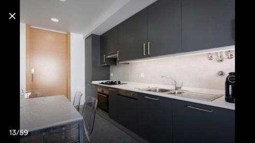 eine Küche mit schwarzen Schränken, einem Waschbecken und einem Tisch in der Unterkunft Modern Apartment for Family and Group of Friends in Sacavém