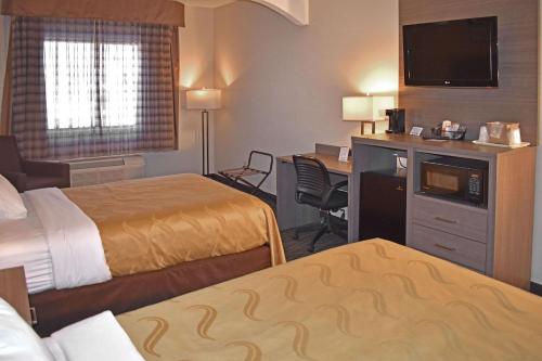 a hotel room with two beds and a desk at Quality Suites Martinsburg in Kearneysville