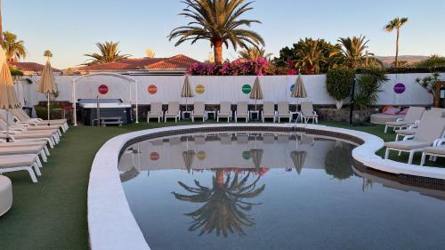 a pool with chairs and umbrellas in a resort at Rainbow Golf Bungalows, Gay Men-only Resort in Maspalomas