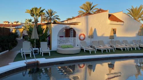 a villa with a swimming pool in front of a house at Rainbow Golf Bungalows, Gay Men-only Resort in Maspalomas