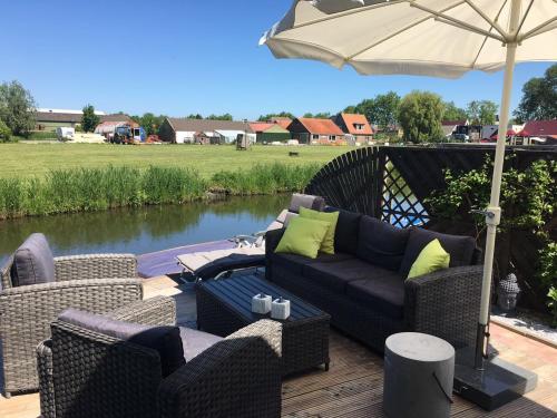 une terrasse avec un canapé, des chaises et un parasol dans l'établissement Holzhaus St.Pauli mit Steg und Wasseblick, à Wervershoof