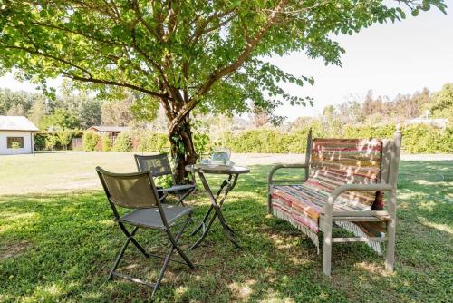 a table and two chairs and a bench under a tree at Casa Galpón en la Laguna de Aculeo in Paine