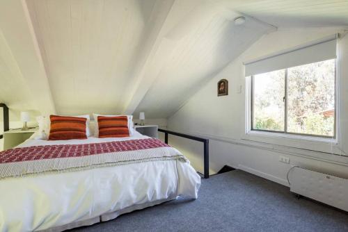 a bedroom with a bed with orange pillows and a window at Casa Galpón en la Laguna de Aculeo in Paine