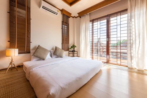 a bedroom with a large white bed and large windows at Hoteru House Ranong 2 - โฮเตรุ เฮ้าส์ ระนอง in Ranong