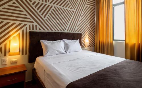 a bedroom with a large white bed with a striped wall at Hotel Rio Blanco in Piura