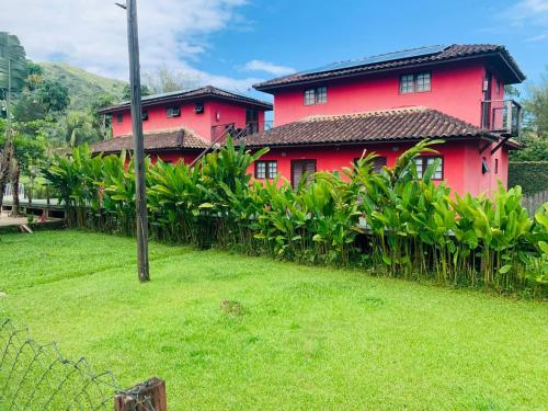 a red house with a green yard in front of it at Chales Terra Pura in Camburi