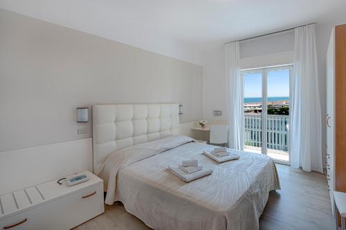 a white bedroom with a large bed and a balcony at Hotel Sanremo in Milano Marittima