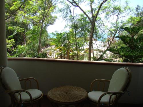 a balcony with two chairs and a table and trees at Hotel Village Eden in Capo Vaticano
