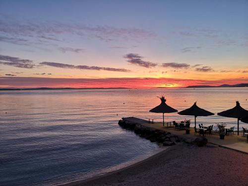 una spiaggia con tavoli e ombrelloni al tramonto di Mintos Luxury Resort a Podstrana