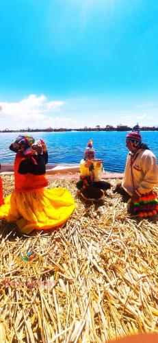 three people sitting on the grass near the water at Uros Maya Lodge in Puno