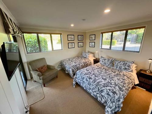 a bedroom with two beds and a chair and windows at Heaven's Rest B&B in Pukekohe East