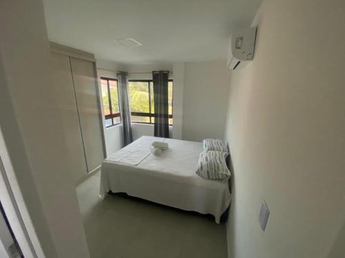 a small white bedroom with a bed and a window at Apartamento Luxo no coração de Porto 103 in Porto De Galinhas