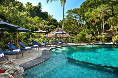a pool with chairs and umbrellas in a resort at Hotel Tjampuhan Spa in Ubud