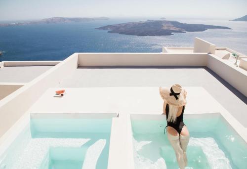 Una donna con un cappello è seduta in piscina di Caldera Cliff Illusion a Firà