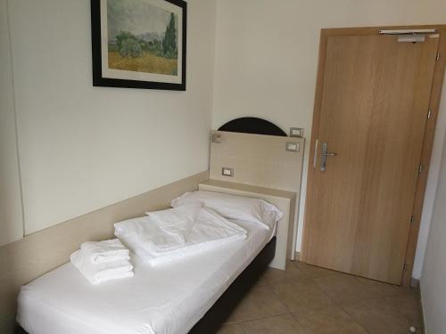 Habitación con cama con sábanas blancas y puerta de madera. en Hotel Sirena, en Malcesine