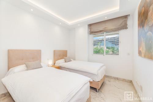2 łóżka w białym pokoju z oknem w obiekcie LetsMarbella - NEW 2BR APARTMENT IN PUERTO BANUS - POOL & PARKING w Marbelli