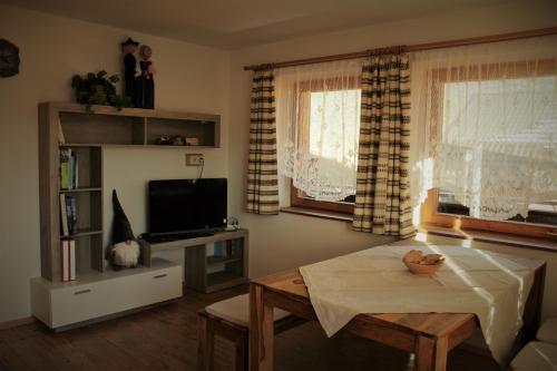 a living room with a table and a tv and two windows at Lü de Terza in San Vigilio Di Marebbe